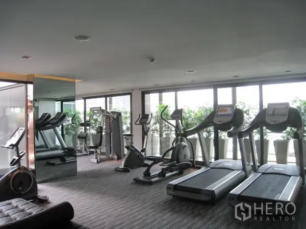 Condominium for rent in Watthana, Bangkok - Light-filled fitness room with treadmills, exercise bikes, weight machines and floor-to-ceiling windows.