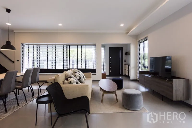 联排别墅 出租在Samut Prakan - 温馨客厅，沙发、电视柜与大窗百叶。