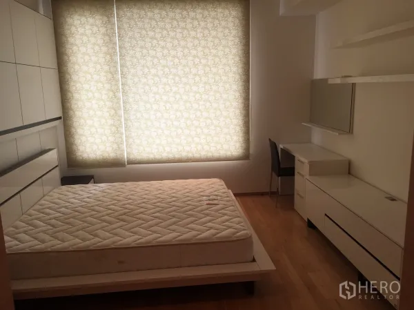 Condominium for rent in Sathon, Bangkok - Second bedroom with a large window, patterned blackout blinds, white built-ins, and a work desk.