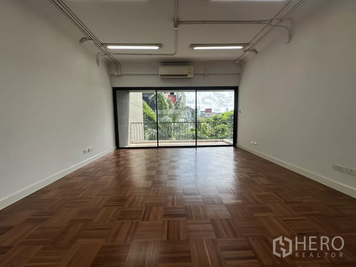 办公空间 出租在Watthana, Bangkok - 开放式办公区，拼花木地板，分体空调，落地推拉门通向阳台，可见城市与绿意景观。