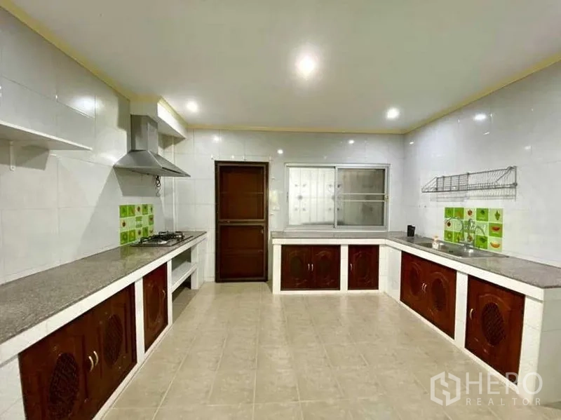 Detached House for sale in Phasi Charoen, Bangkok - Spacious Thai‑style kitchen with L‑shaped countertops, stove and hood, tiled walls, and window ventilation.