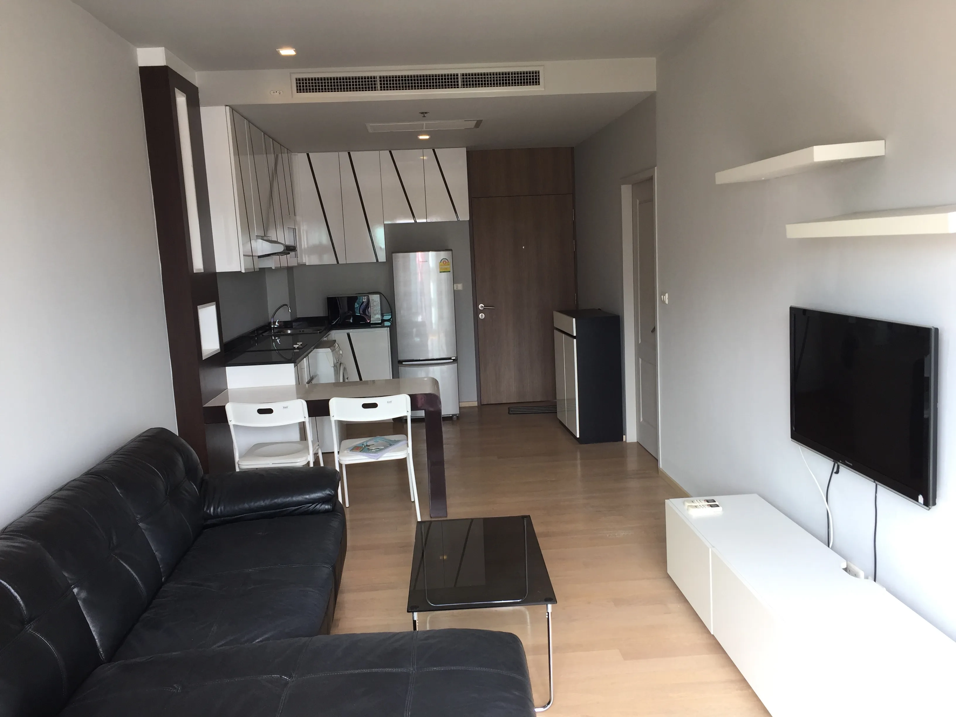 คอนโด ให้เช่าในBangkok - ภายในคอนโดทันสมัย โซนนั่งเล่น ทีวีติดผนัง โต๊ะทานอาหาร และตู้ครัวสีขาวเรียบหรู.