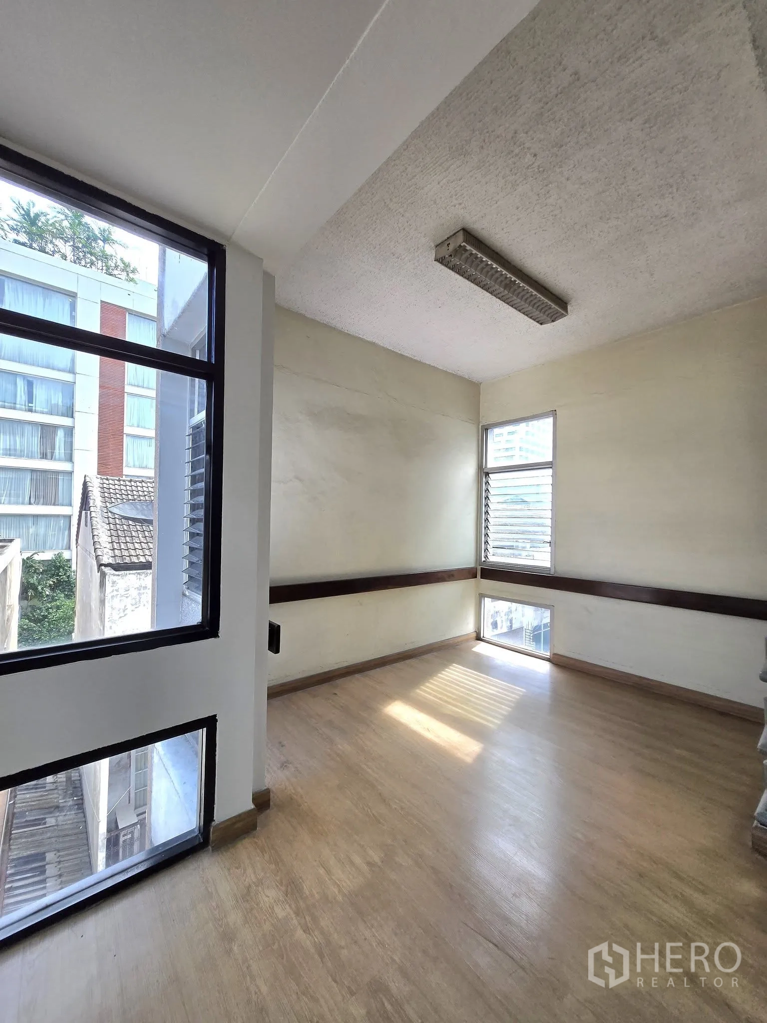 Office Space for rent in Khlong Toei, Bangkok - Small corner office with windows on two sides, wood flooring, and daylight.