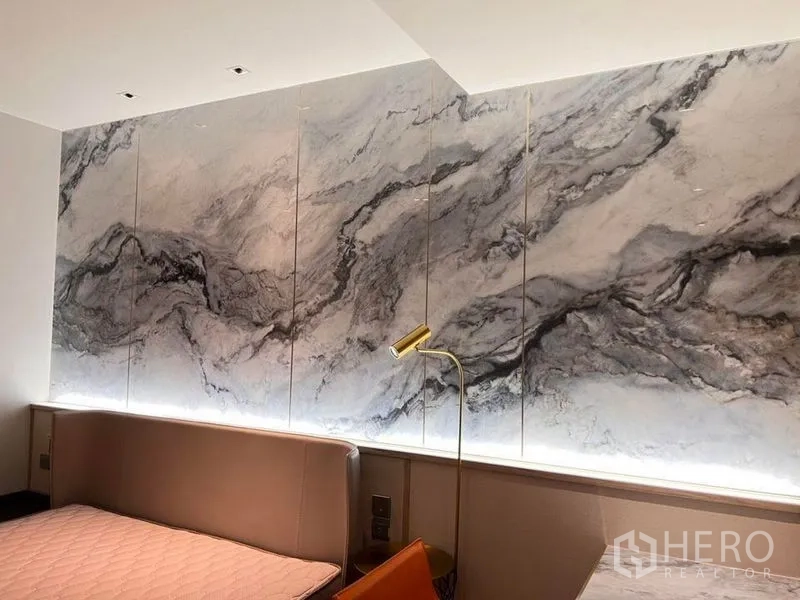 Condominium for rent in Khlong Toei, Bangkok - Feature marble wall with warm backlighting above a headboard, paired with a brass reading lamp.