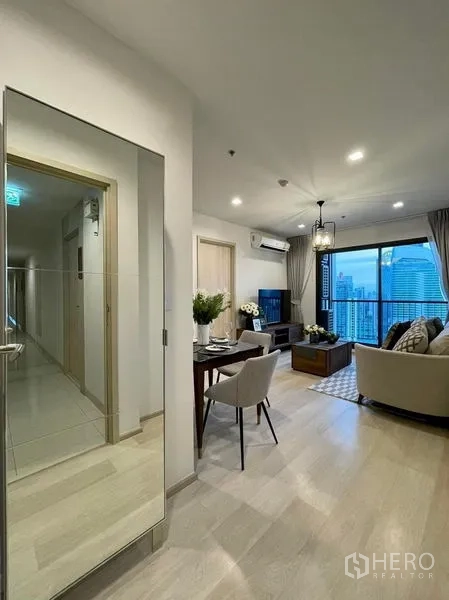 Condominium for rent in Pathum Wan, Bangkok - Entry corridor with full-height mirror leading to bright living room and balcony city view.