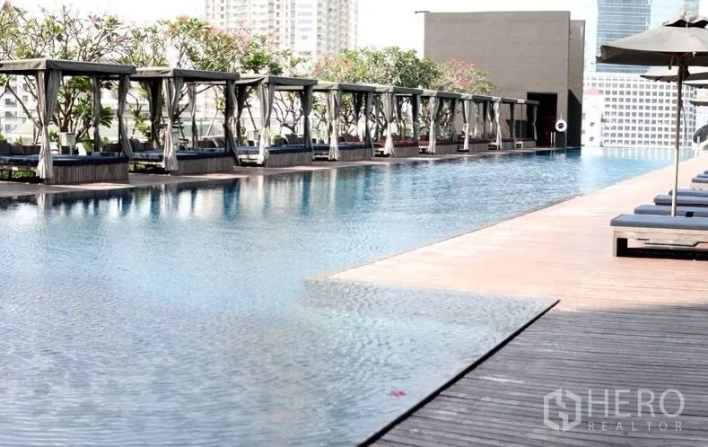 Condominium for rent in Sathon, Bangkok - Rooftop lap pool with cabanas and city views on a wooden deck.