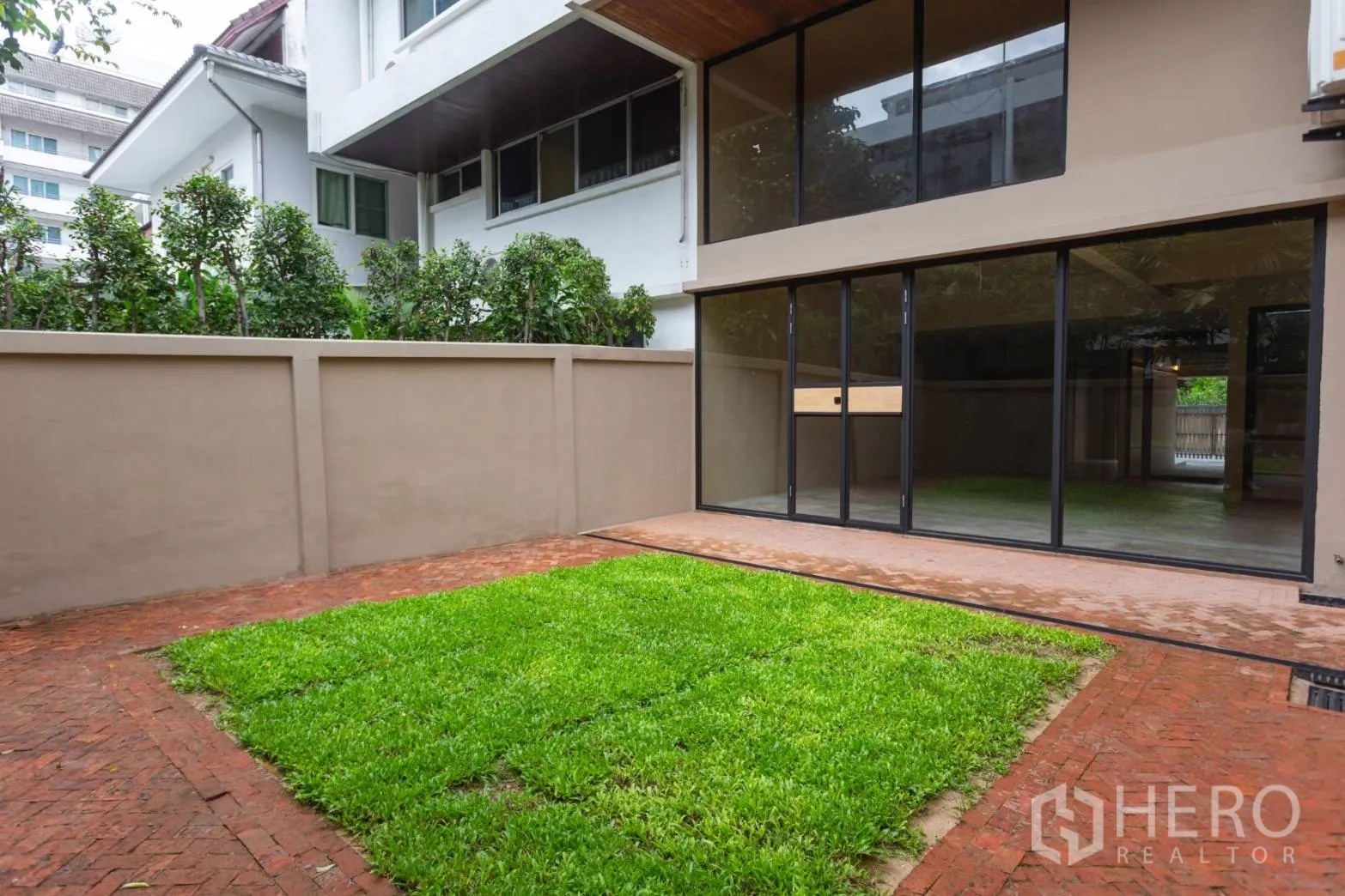 Home Office for rent in Watthana, Bangkok - Rear exterior showing full‑height glazing opening to lawn courtyard.