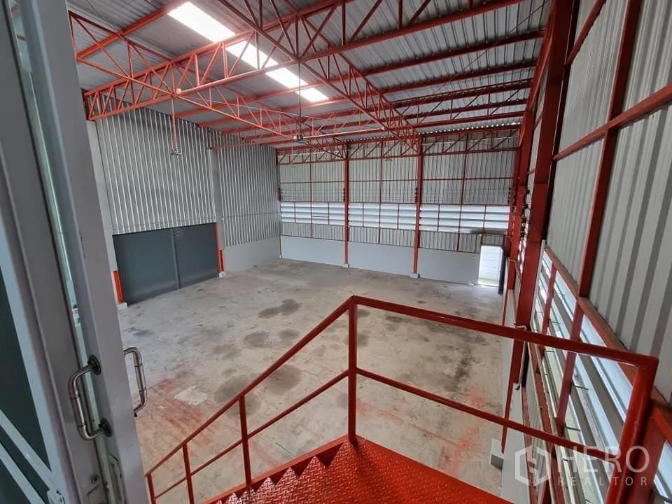 คลังสินค้า ให้เช่าในLam Luk Ka, Pathum Thani - มุมมองจากบันไดชั้นลอยลงสู่โกดังเพดานสูงและโครงหลังคาเหล็ก