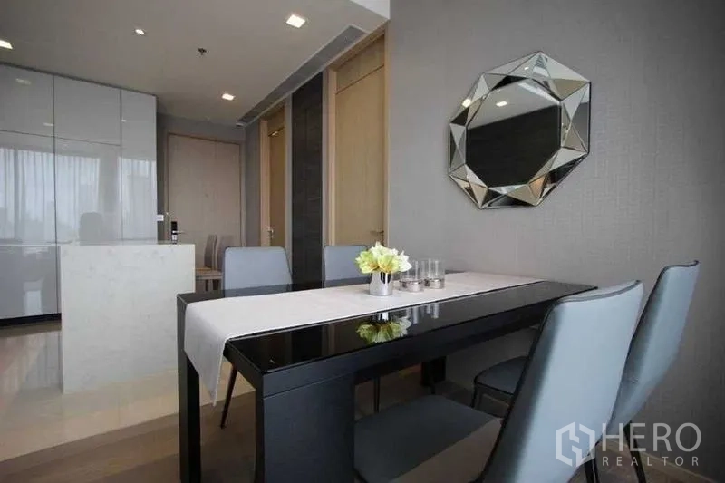 Condominium for rent in Watthana, Bangkok - Dining nook with four chairs, glossy black table and geometric wall mirror.