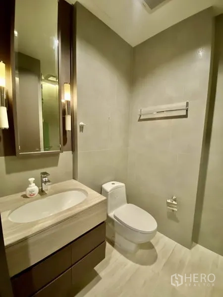 Condominium for rent or sale in Bang Rak, Bangkok - Guest bathroom with vanity, toilet and neutral tiles with sconce lighting.