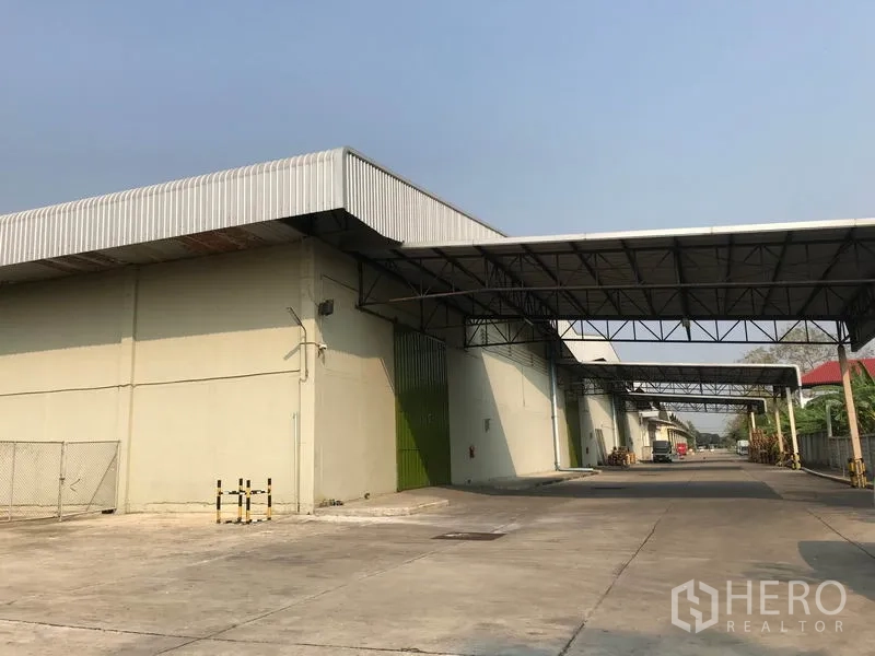 货栈 出租在Bang Pa-in, Phra Nakhon Si Ayutthaya - 仓库立面，多个绿色卷门与连廊雨棚，卡车通道笔直