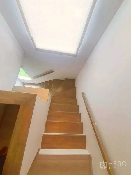 Detached House for sale in Samut Prakan - Wooden staircase with handrail and skylight bringing natural light.