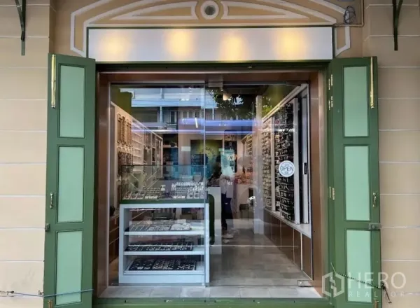 零售空间 出租在Samphanthawong, Bangkok - 玻璃临街店面，绿色百叶窗与明亮招牌，内有商品陈列。