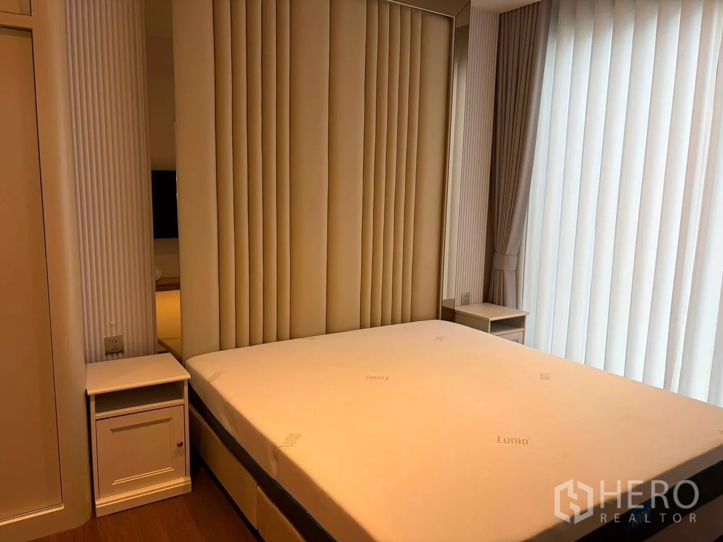 Condominium for rent in Watthana, Bangkok - Bedroom with upholstered headboard, bedside tables, and floor-to-ceiling curtains.