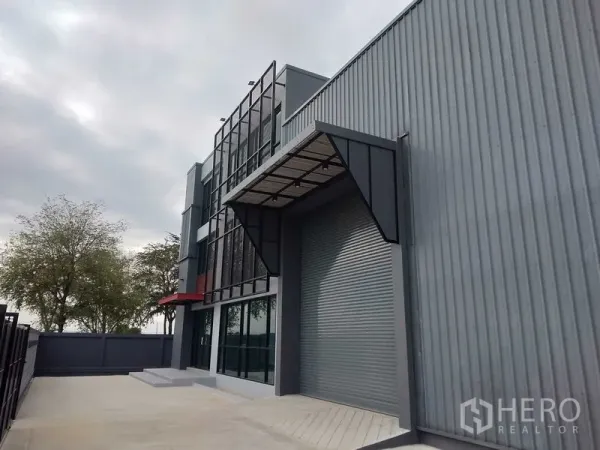Factory for rent or sale - Warehouse loading bay featuring a large roll-up door and metal canopy beside the glass-fronted office building.