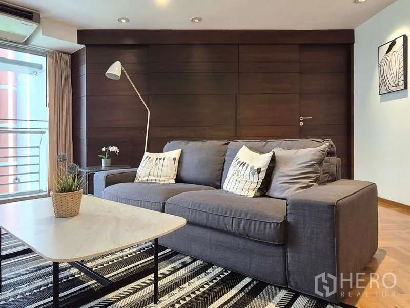 Condominium for rent in Yan Nawa, Bangkok - Cozy living room corner with gray sofa, marble-top table and balcony door.