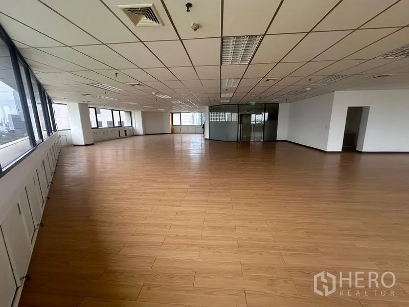 办公空间 出租在Bang Rak, Bangkok - 开阔开间办公室，木纹地板、格栅吊顶照明与城市景观窗。
