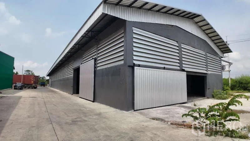Warehouse for rent in Chachoengsao - Corner view with multiple loading doors, louvered walls and a truck access lane beside the building.