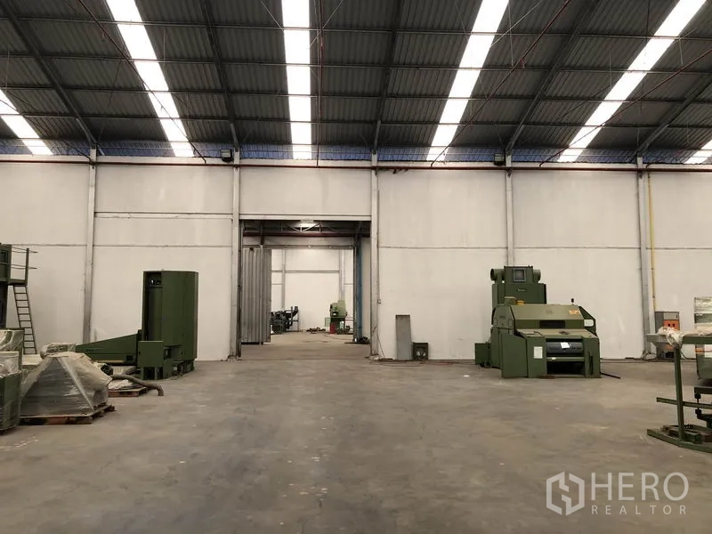Warehouse for rent in Bang Bua Thong, Nonthaburi - Spacious factory-style interior with skylights and industrial machines on concrete floor.