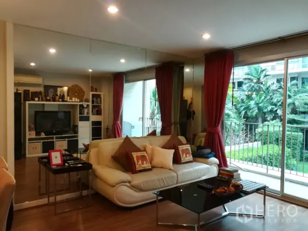 Condominium for rent in Watthana, Bangkok - Cozy living room with cream sofa, coffee table and balcony facing a green courtyard.
