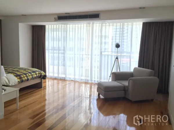 Condominium for rent in Watthana, Bangkok - Spacious master bedroom with sheer curtains, wooden flooring and a lounge chair with ottoman.