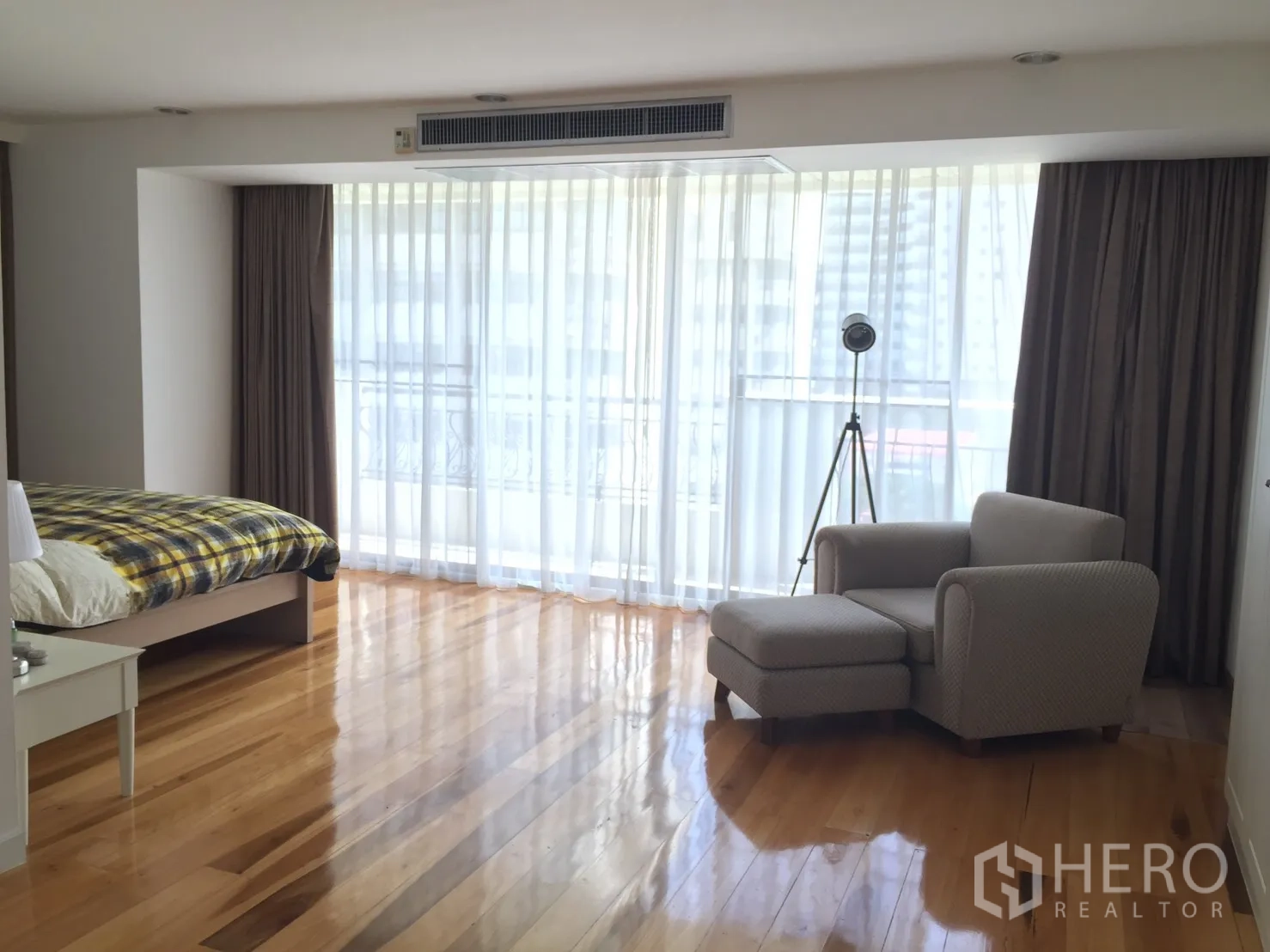 Condominium for rent in Watthana, Bangkok - Spacious master bedroom with sheer curtains, wooden flooring and a lounge chair with ottoman.