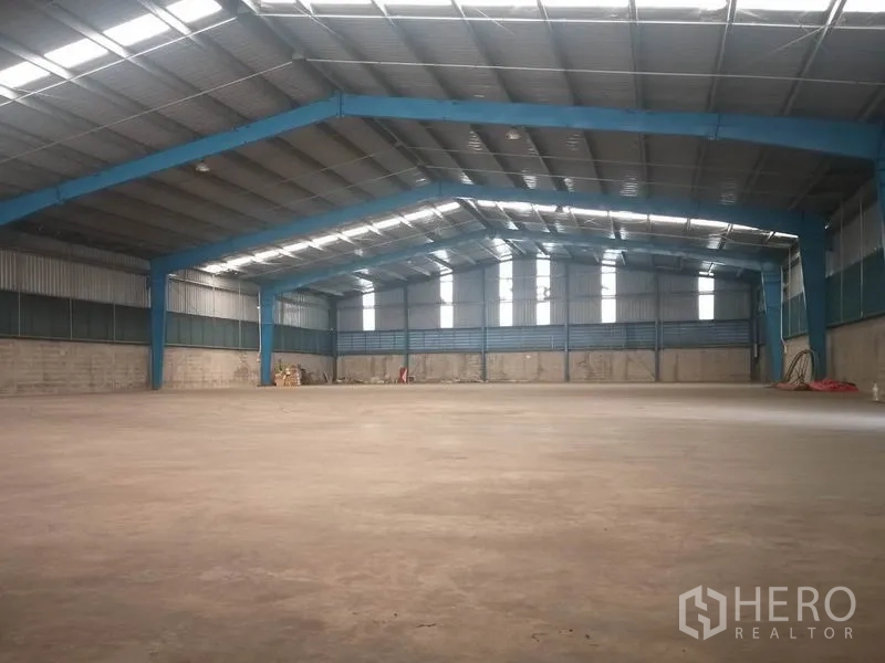 Warehouse for rent in Pathum Thani - Spacious warehouse interior with high steel frame, skylights, and open floor.