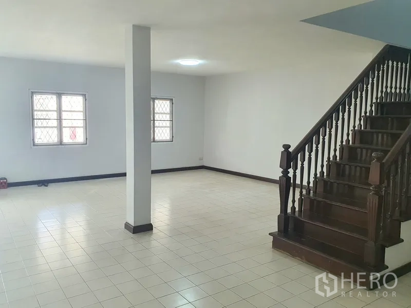 联排别墅 出售在Khlong Toei, Bangkok - 开放式客餐区，中央立柱，瓷砖地面与深色木楼梯。