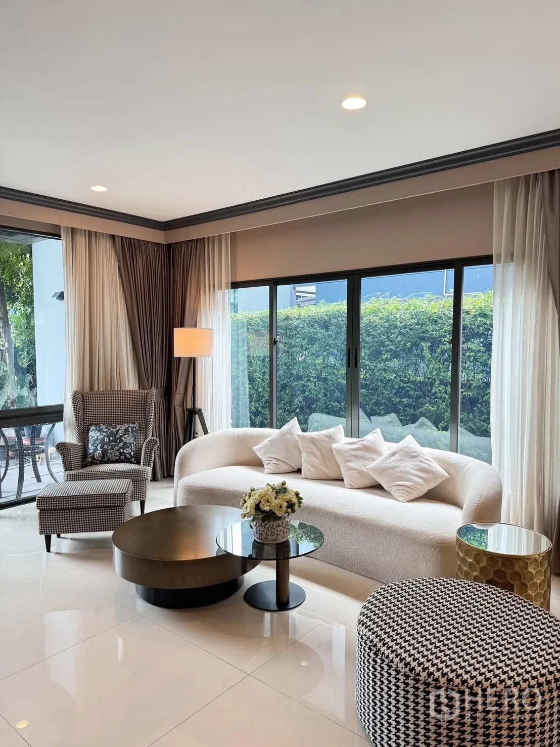 บ้านเดี่ยว for rent in Bang Kapi, Bangkok - มุมนั่งเล่นสว่างด้วยโซฟาทรงโค้ง พัฟลายฮาวนด์ทูธ และวิวสวนผ่านหน้าต่างบานใหญ่