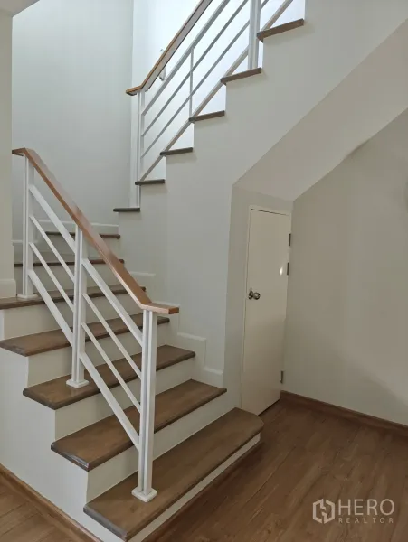 联排别墅 出租或出售在Lat Phrao, Bangkok - 木踏步楼梯配白色扶手，楼梯下方设储物柜。