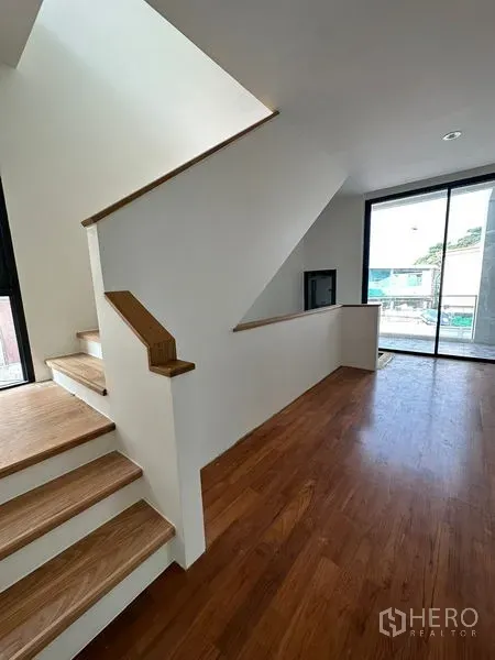 独立式住宅 出租在Watthana, Bangkok - 现代木质楼梯通往明亮的楼梯平台，推拉门连接室外阳台。