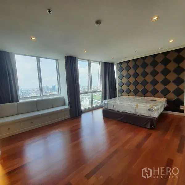 Condominium for rent in Bang Kapi, Bangkok - Large corner bedroom with wood flooring, padded feature wall, built-in bench seating and wide city-view windows.
