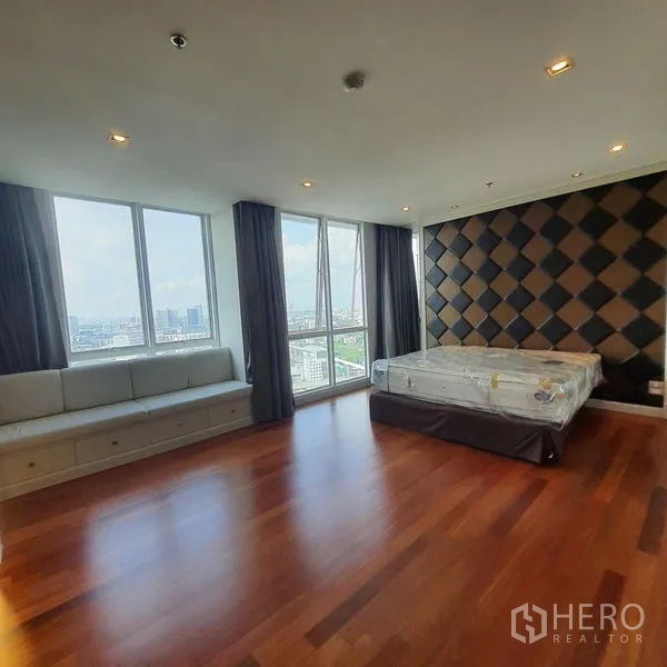 Condominium for rent in Bang Kapi, Bangkok - Large corner bedroom with wood flooring, padded feature wall, built-in bench seating and wide city-view windows.