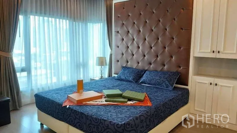 Condominium for rent in Khlong Toei, Bangkok - Bedroom with floor-to-ceiling windows, drapes and upholstered headboard.