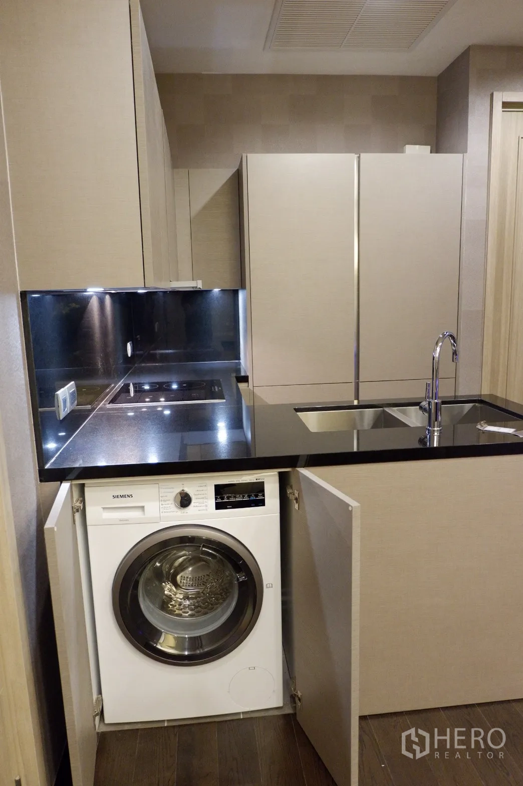 Condominium for rent in Watthana, Bangkok - Modern kitchenette with black stone countertop, induction hob, sink and built-in washing machine in a Phrom Phong condo.