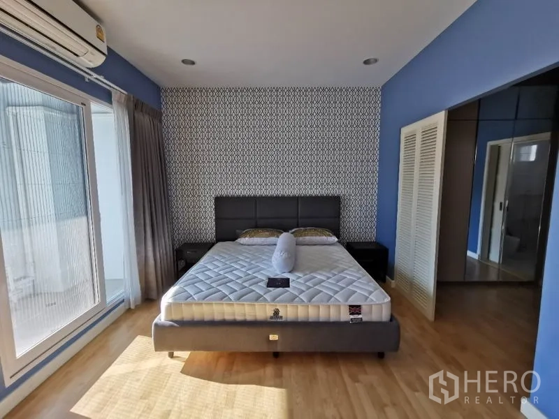 联排别墅 出租在Wang Thonglang, Bangkok - 主卧采光充足，灰色床架、图案背景墙与阳台玻璃门。