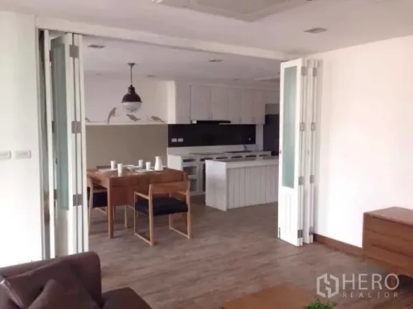 Condominium for rent in Huai Khwang, Bangkok - Open-plan dining area and white kitchen with island and folding doors over wood floors.