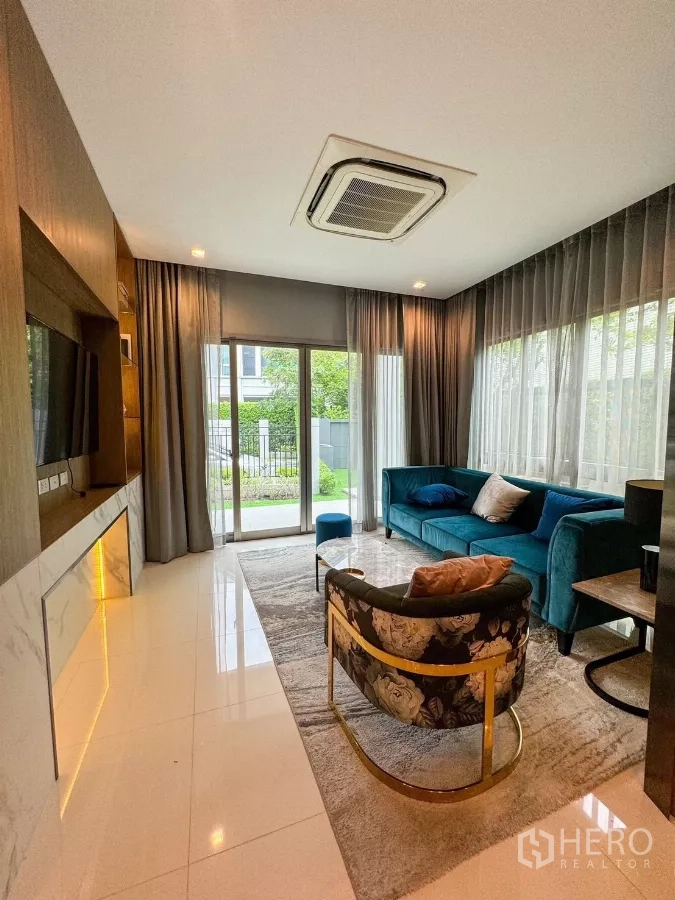 Detached House for rent or sale in Bueng Kum, Bangkok - Bright living room with teal sofa, floor-to-ceiling windows and view to the front garden.