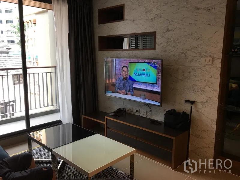 Condominium for rent in Watthana, Bangkok - Living room with marble feature wall, wall-mounted TV, glass coffee table and balcony access.