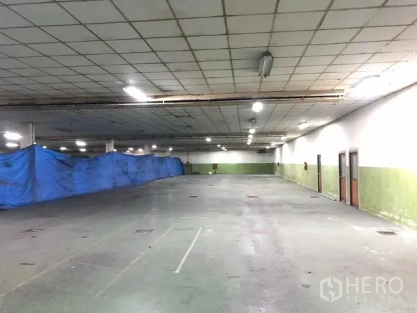 โรงงาน ให้เช่าในLat Krabang, Bangkok - พื้นที่ภายในโรงงานโล่งกว้าง มีผ้าใบสีน้ำเงินกั้น ช่องระบายน้ำ และประตูด้านข้างหลายจุด