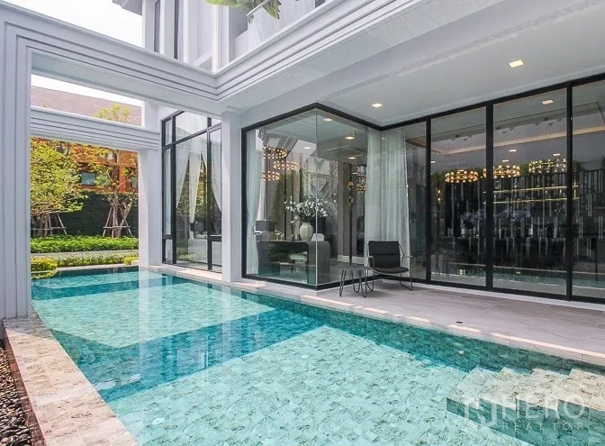 Detached House for rent or sale in Prawet, Bangkok - Private swimming pool beside a glass-walled modern house with landscaped garden.