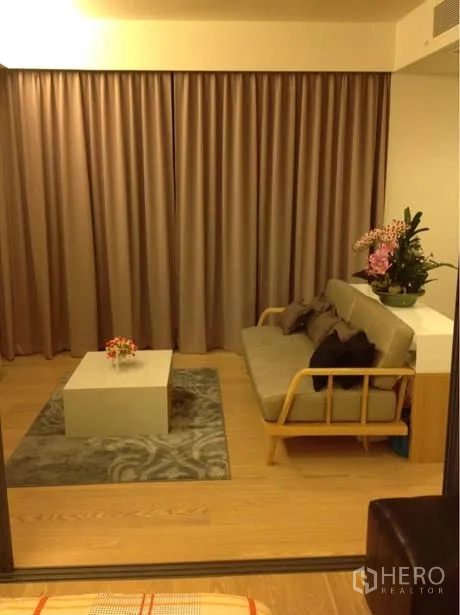 Condominium for rent or sale in Watthana, Bangkok - Lounge area with sofa, coffee table and full-length curtains