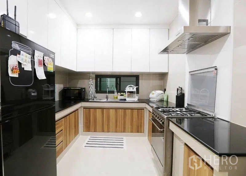 Detached House for rent or sale in Bang Kapi, Bangkok - U-shaped modern kitchen with white cabinetry, wood accents, gas stove and stainless hood.