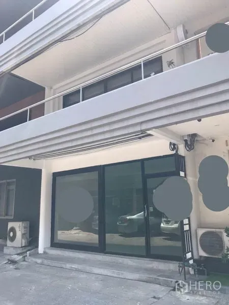 零售空间 出租在Watthana, Bangkok - 更广角外立面，低层建筑，玻璃门面与上层露台，可见室外空调机与停车区域。