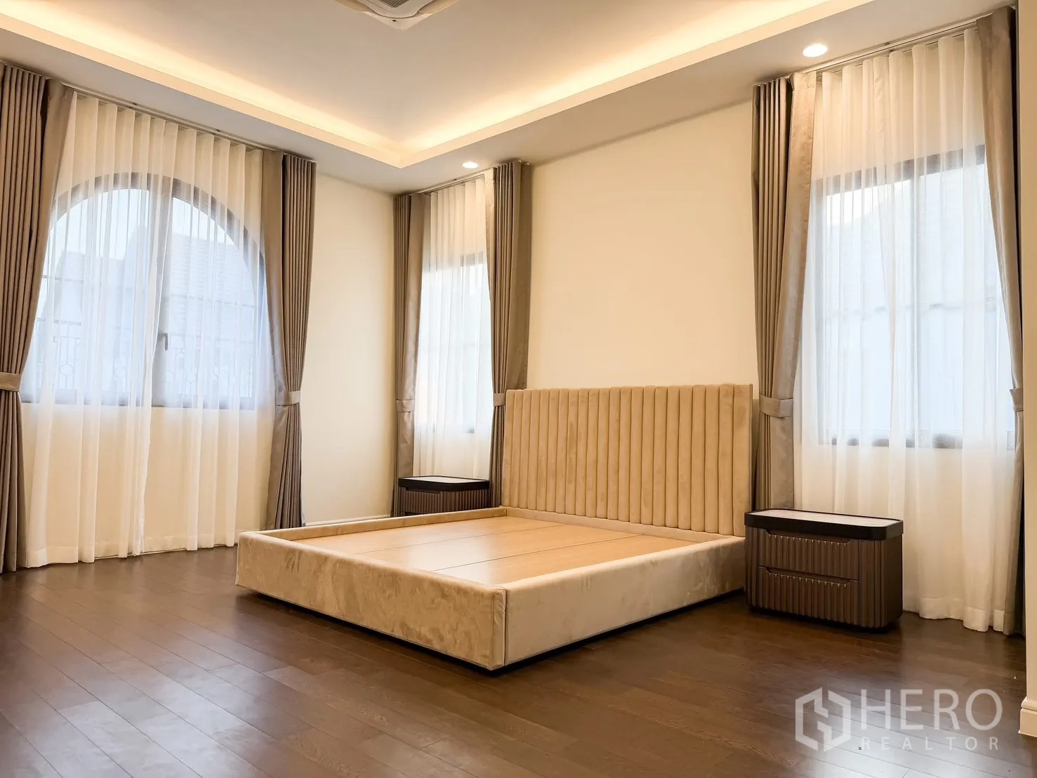 บ้านเดี่ยว for rent in Bang Khen, Bangkok - ห้องนอนกว้าง เตียงบุนวมสีน้ำตาลอ่อน ฝ้าหลุมไฟซ่อน และหน้าต่างหลายบาน.