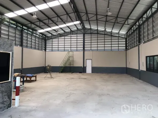 货栈 出售在Pathum Thani - 库内广角视图，通风板、吊灯、窗户及一侧绿色金属楼梯。