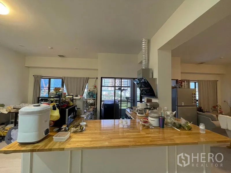 Condominium for sale in Sathon, Bangkok - Functional kitchen with a long wooden countertop, cooktop, range hood and sliding doors to a balcony.