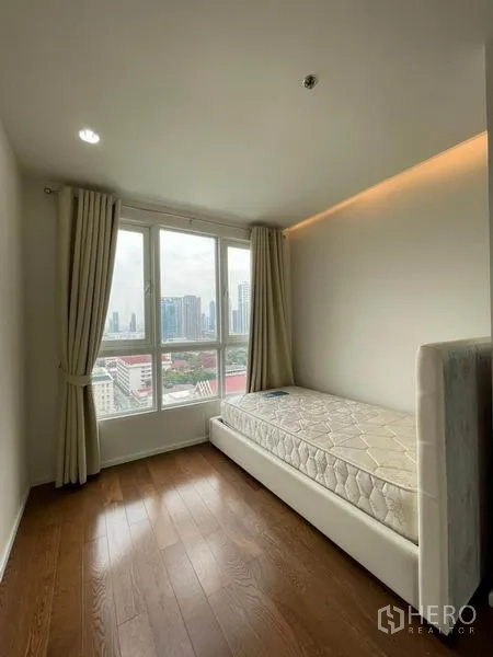 คอนโด ให้เช่าหรือขายในWatthana, Bangkok - ห้องนอนรองสว่างพร้อมเตียงเดี่ยว พื้นไม้ และหน้าต่างบานใหญ่เห็นวิวสกายไลน์กรุงเทพฯ