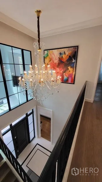 Detached House for rent or sale in Saphan Sung, Bangkok - Crystal chandelier above the upper landing with colorful artwork and black railings.