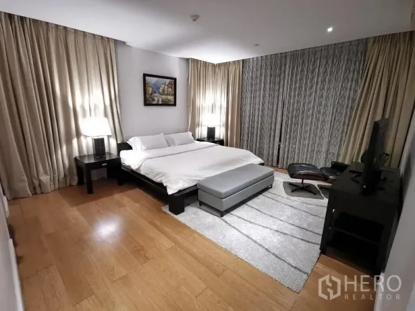 Condominium for rent in Watthana, Bangkok - Primary bedroom with king bed, wood floors, large windows, and a lounge chair.